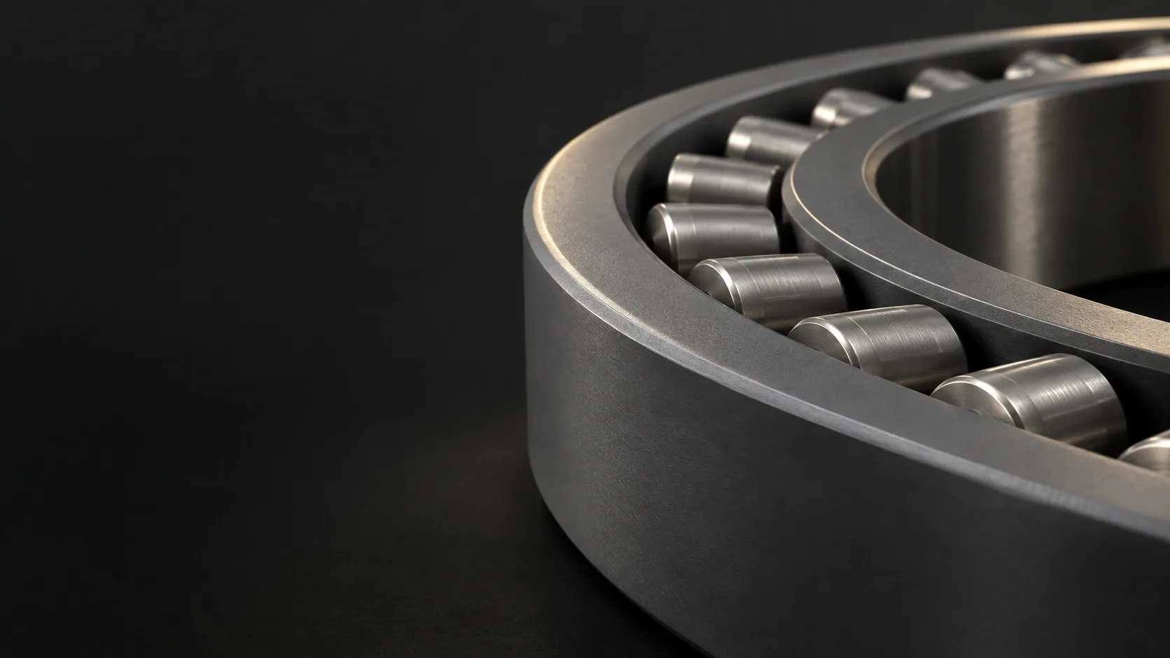 A studio close-up of a grey roller bearing and its circular race against a dark graphite background